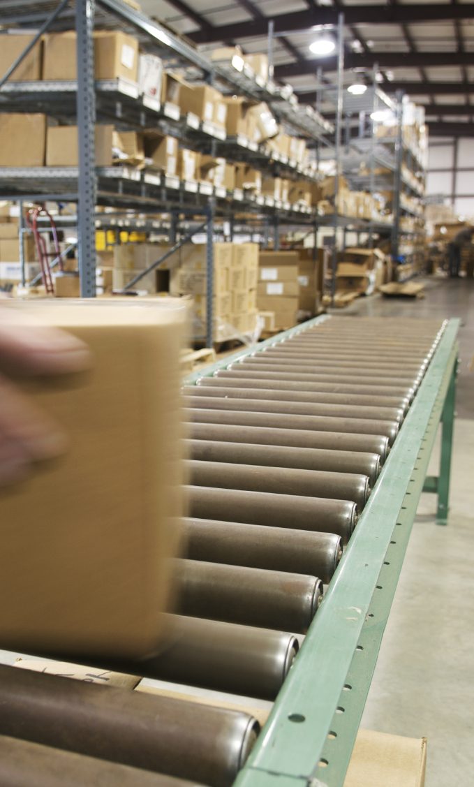 Almacén Mano colocando una caja en una cinta transportadora en un almacén lleno de estanterías.