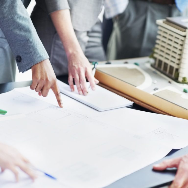 Equipo de trabajo Manos señalando planos y maquetas en una mesa de trabajo.